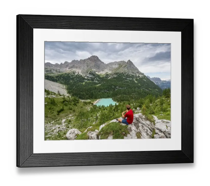 Framed Print : Young man, hiker sitting on rocks and looking at turquoise green Sorapis lake and mountain landscape
