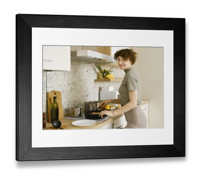 Framed Print : Smiling woman puts cooked pasta with mushroom sauce from a frying pan on a plate