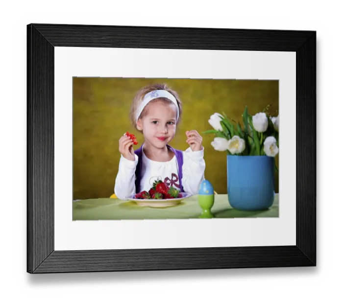 Framed Print : Little blonde girl eating strawberries at a table