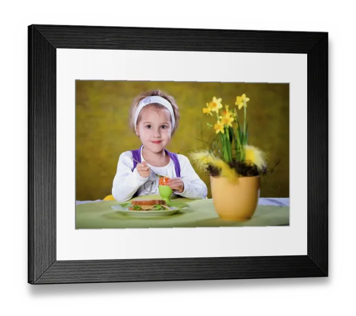 Framed Print : Little girl eating an Easter egg at a table