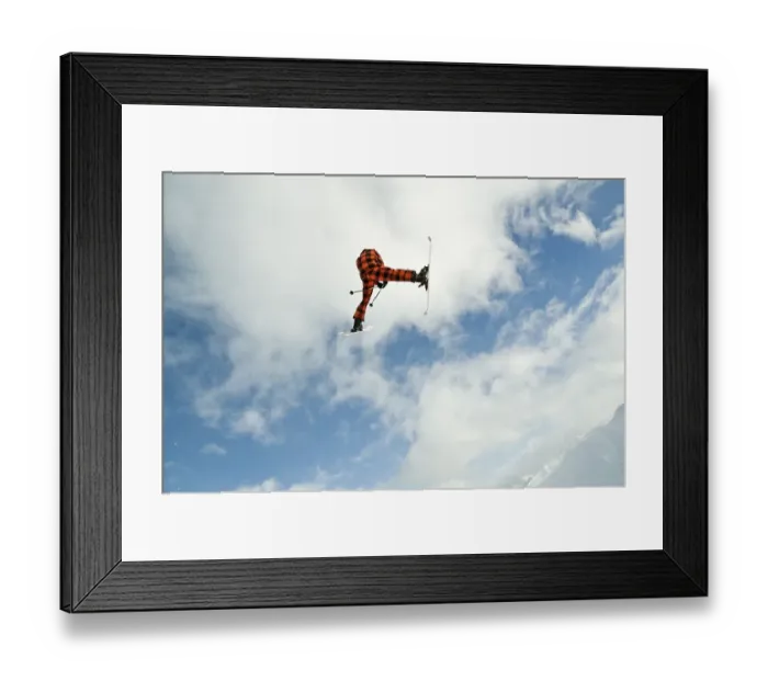 Framed Print : Skier jumping in front of a blue sky with a snow-covered mountain range behind