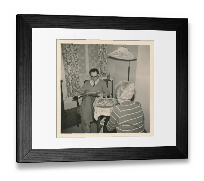 Framed Print : Christmas 1956: A married couple sits at a small table with a candle and Christmas biscuits on top