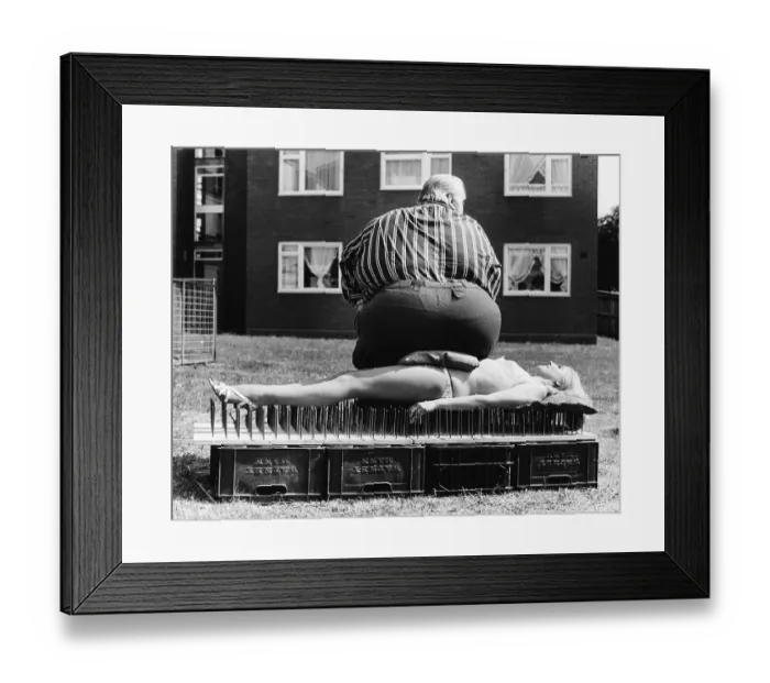 Framed Print : Thick man sitting on a woman lying on nail board