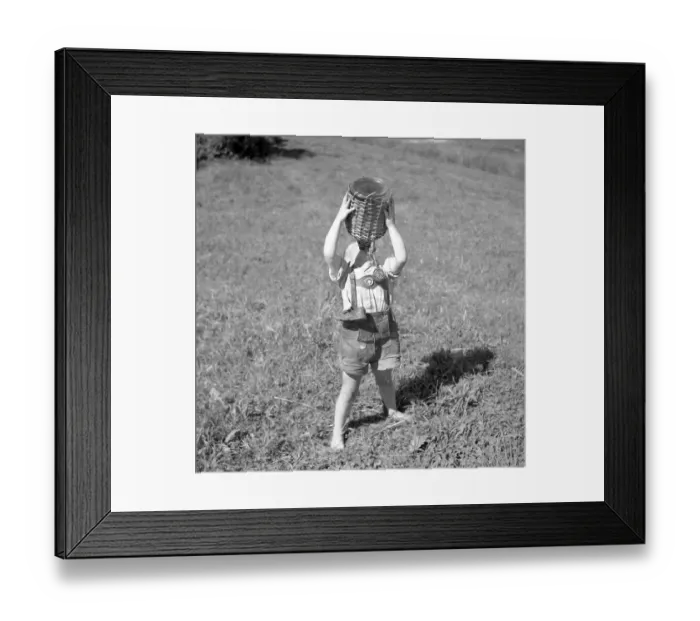 Framed Print : Child stands barefoot in a meadow and drinks water from a wooden-coated vessel
