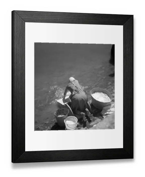 Framed Print : Woman washes her clothes in an old-fashioned way in the river around 1950