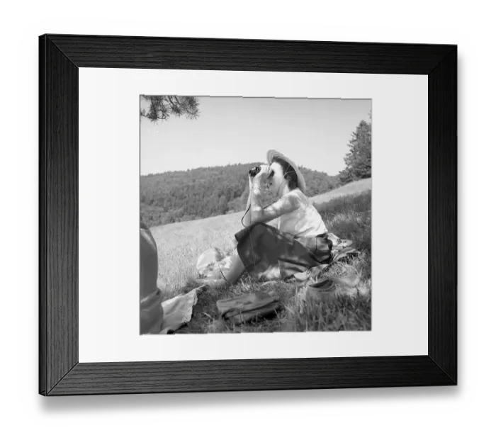 Framed Print : Woman sitting in nature looking through binoculars around 1950