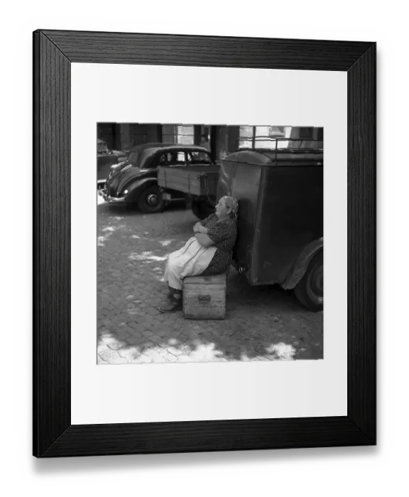 Framed Print : Woman sitting on a wooden box and leaning against a car