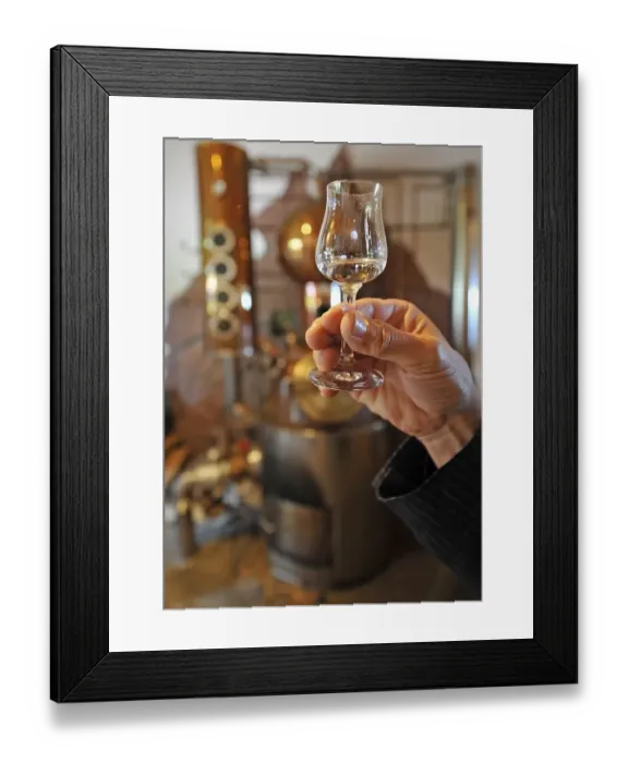 Framed Print : Hand holding jigger in front of a distillery