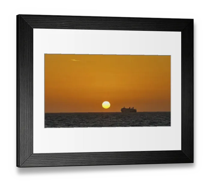Framed Print : A ferry sails in front of a bright orange sky at sunset on the sea