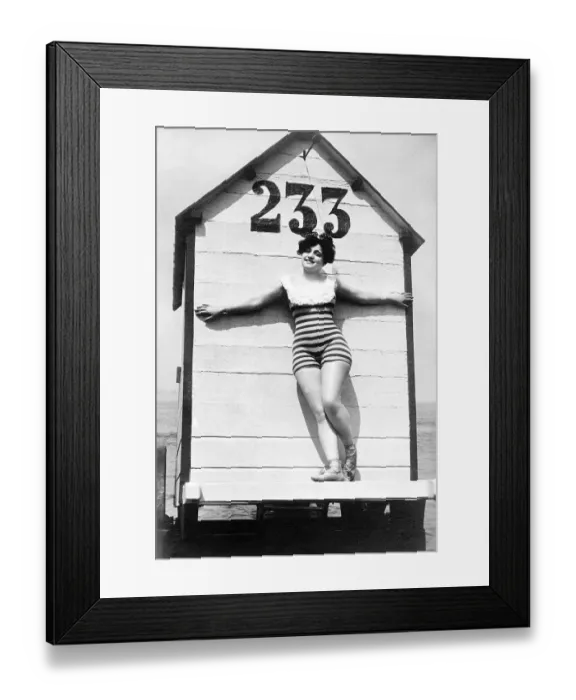 Framed Print : Woman in swimsuit posing in front of a historic dressing room on the beach