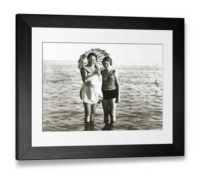 Framed Print : Two women in swimsuits and with parasol standing in the sea