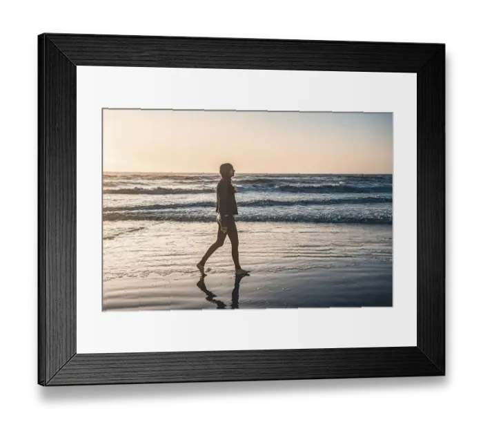 Framed Print : A lonely woman at the beach walking barefooted by the shore at sunrise