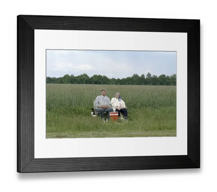 Framed Print : A couple of pensioners sitting on folding chairs at the edge of a field