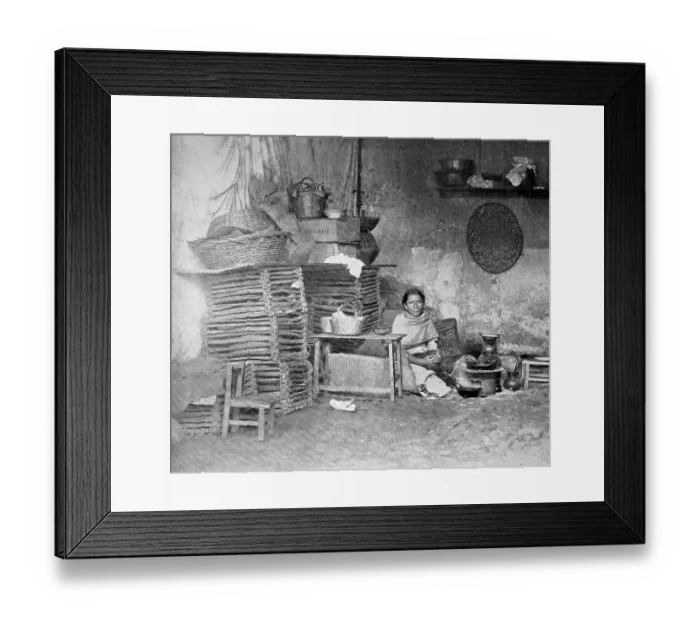 Framed Print : Poor Mexican woman sitting in her kitchen at the charcoal kettle and next to her is a stack of woven baskets