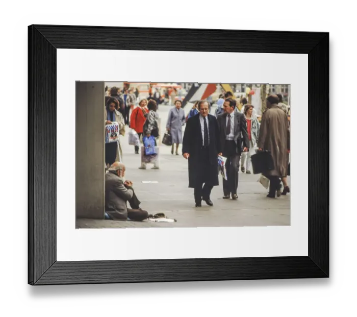 Framed Print : Beggar sitting on the ground on Schlossplatz with passers-by
