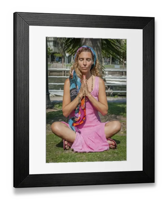 Framed Print : Young woman sitting cross-legged while meditating with her hands clasped outdoors