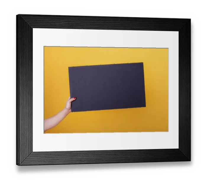 Framed Print : Female hand holding a blank black sheet poster for copy-space and mockup on a yellow background