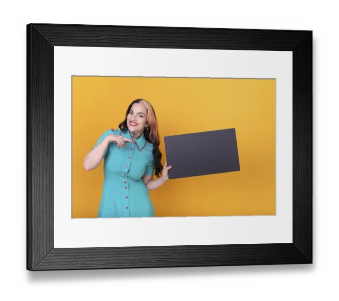 Framed Print : Beautiful woman pointing at a blank black board against a yellow background Framed Print : Beautiful woman pointing at a blank black board against a yellow background