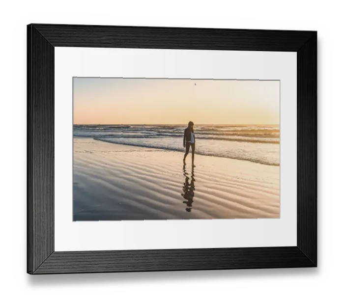 Framed Print : A lonely woman at the beach walking barefooted by the shore at sunrise