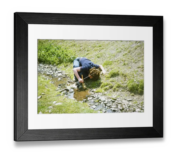 Framed Print : Secondary school student doing geographical fieldwork, Great Britain 1970s: Girl measuring the depth of a small stream with a ruler, 1977