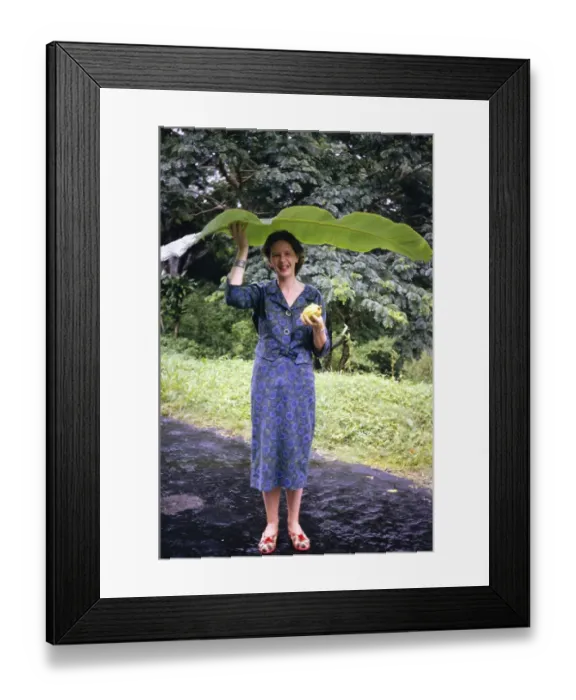 Framed Print : Woman sheltering from rain beneath large banana leaf, Trinidad 1963