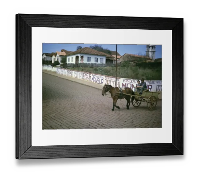 Framed Print : Man and boy riding on a horse-drawn cart past election campaign posters of politician Joao Mansur (1923 2012), Palmeira, Parana state, Brazil 1962
