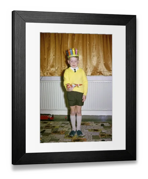 Framed Print : Kleiner Junge mit gelbem Pullover und rotem Indianerhut spielt am Weihnachtsmorgen mit einer roten Weltraumrakete, britische Kultur 1967