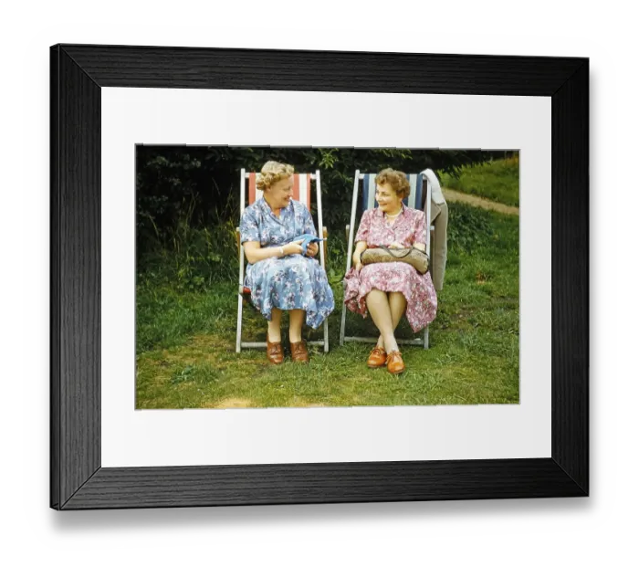 Framed Print : Two women friends sitting in deckchairs on grass lawn one knitting, smiling at each other, England, UK early 1960s