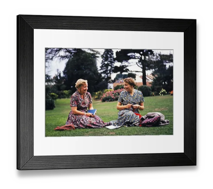 Framed Print : Two women friends sitting on grass lawn one knitting, smiling at each other, Dawlish, Devon, England, UK early 1960s