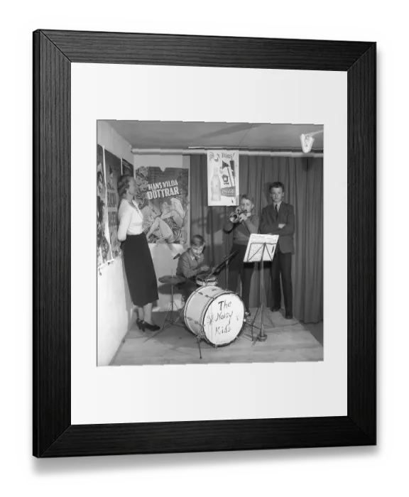 Framed Print : The Noisy Kids 1956. A drummer and a trumpeter are playing on a simple stage. On the wall behind them are film posters and advertisements for Coca-Cola. A woman stands to the side, listening Framed Print : The Noisy Kids 1956. A drummer and a trumpeter are playing on a simple stage. On the wall behind them are film posters and advertisements for Coca-Cola. A woman stands to the side, listening