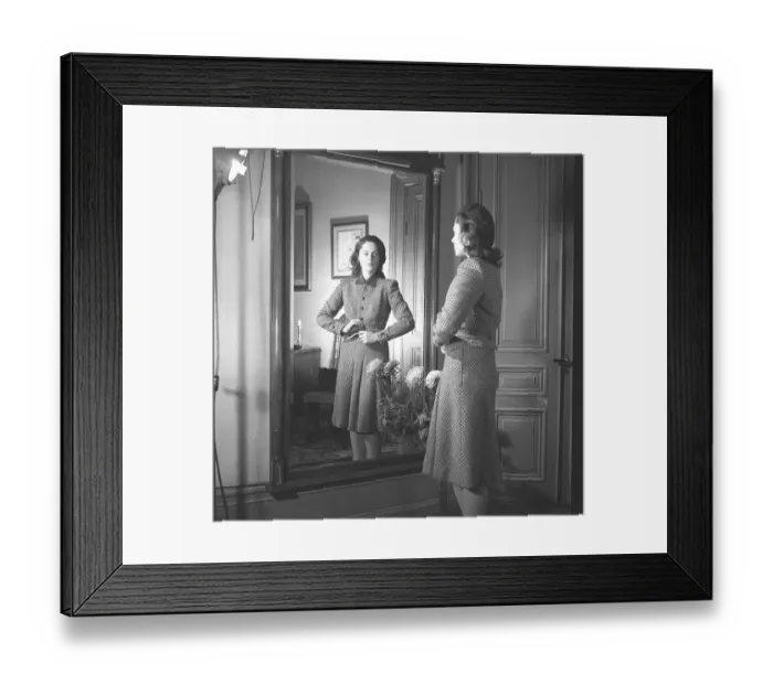 Framed Print : Actress Viveca Lindfors, 1920-1995. She stands in front of the mirror and buttons the last button of her plaid two-piece suit with a knee-length skirt and a waist-length jacket. 1945. Kristoffersson ref R55-6