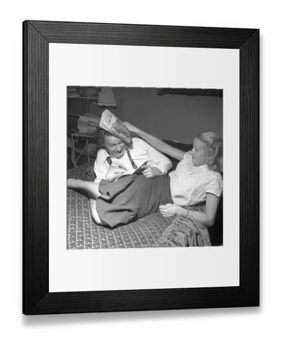 Framed Print : In the 1950s. A young couple at home is seen fighting in a playful manor. She hits him over the head with a book. 1952. Conard ref 2251