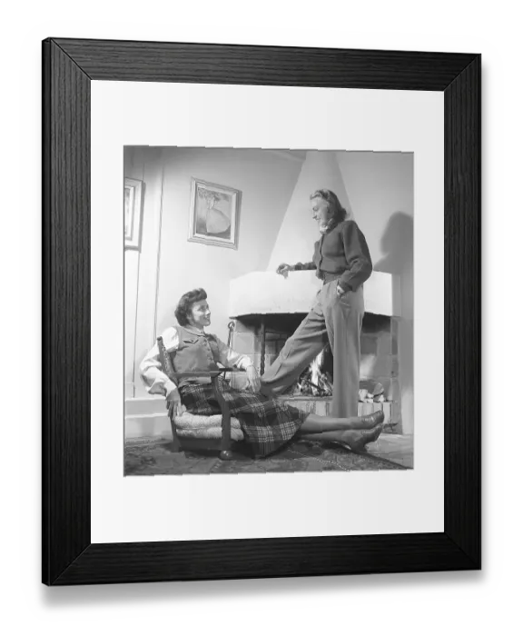 Framed Print : Fashionable in the 1940s. Two women in a room where with a fire burning in the fireplace. One sitting in an extraordinary looking armchair that has no legs. They are both wearing the typical clothes and fashion of the 1940s decade