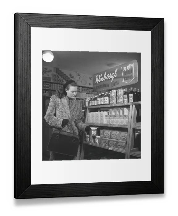 Framed Print : A woman shopping for food in the 1940s. A young woman is shopping in a self-service shop. She takes a closer look at one of Winborg's products, apple sauce Framed Print : A woman shopping for food in the 1940s. A young woman is shopping in a self-service shop. She takes a closer look at one of Winborg's products, apple sauce