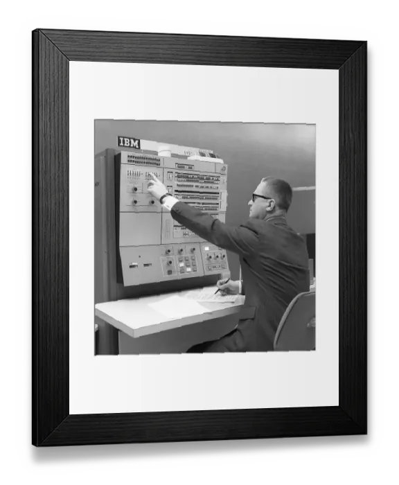 Framed Print : In the 1960s. Interior of a room with computers and people on the job of handling them and register and reading information. A sign above the mainframe computer says IBM 360