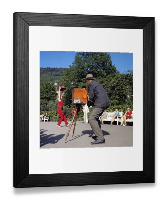 Framed Print : 1960s photographer and model. The actress and singer Grynet Molvig pictured in the norwegian town Bergen, posing for a photographer with his antique camera on a tripod. Grynet is her all red outfit lifts her hat and smiles. 1969