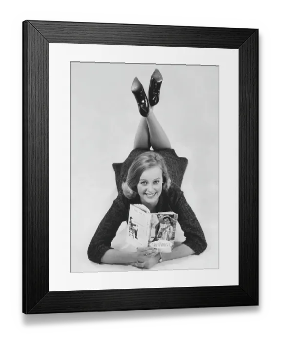 Framed Print : In the 1960s. A young woman lying down with the book by Noel Coward. 1961 Framed Print : In the 1960s. A young woman lying down with the book by Noel Coward. 1961