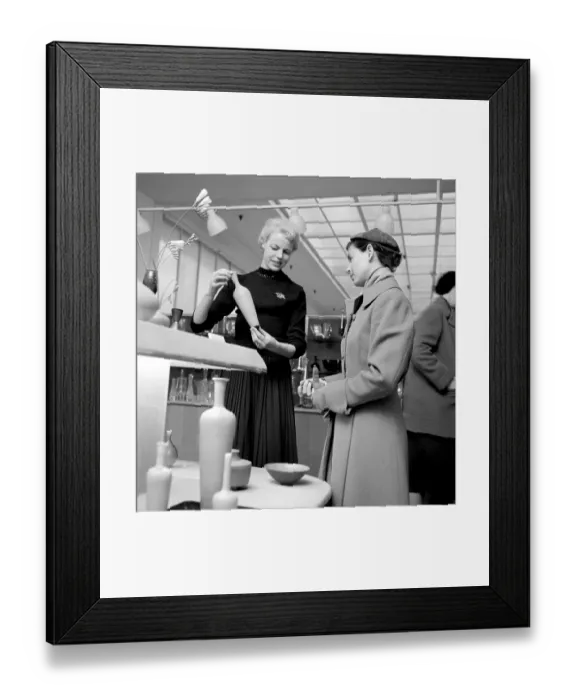 Framed Print : Shopping in the 1950s. A young woman in a store where a sales woman is presenting some of the stores selection of fine cermaics and decorative items designed by the famous designer Stig Lindberg