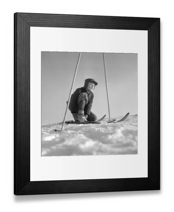 Framed Print : Winter in the 1950s. A boy is seen putting on his skis on a sunny winter day 1950 Framed Print : Winter in the 1950s. A boy is seen putting on his skis on a sunny winter day 1950