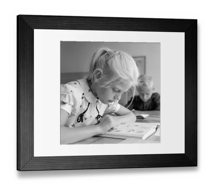 Framed Print : School in the 1950s. A girl is seen sitting at her desk in the classroom reading from the schoolbook in front of her