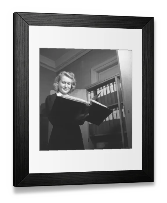Framed Print : Woman in an office in 1942. A young female employee flips through the content of a binder