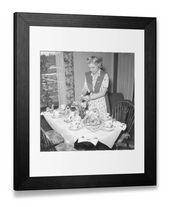 Framed Print : In the 1940s. A woman has set a table for Easter and arranges daffodils to be placed in a vase on the table Framed Print : In the 1940s. A woman has set a table for Easter and arranges daffodils to be placed in a vase on the table