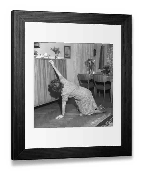 Framed Print : Woman in the past. A woman is kneeling on the floor at home and wiping a dust cloth over the cabinet doors