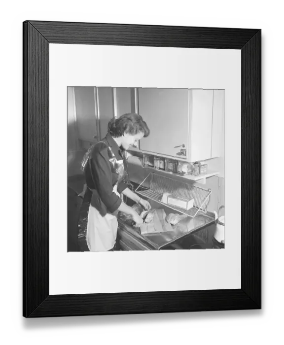 Framed Print : In the kitchen 1950s. Interior of a kitchen and a young woman standing at the kitchen sink preparing the ingredients Framed Print : In the kitchen 1950s. Interior of a kitchen and a young woman standing at the kitchen sink preparing the ingredients