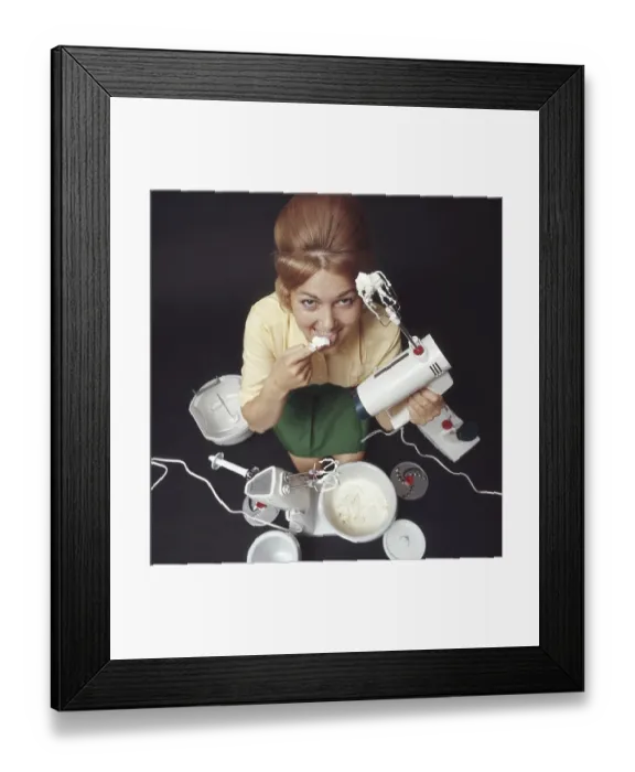 Framed Print : In the 1960s. A young woman pictured with an electric mixer having whipped cream and is tasting it. She is dressed in the typical 1960s colors of clothes and her hair in the popular Beehive hairdo. Sweden 1969. Kristoffersson