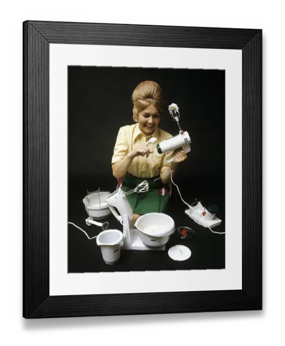Framed Print : In the 1960s. A young woman pictured with an electric mixer having whipped cream and is tasting it. The machine and it's accessories are lined up in front of her demonstrating the different kinds of function it has Framed Print : In the 1960s. A young woman pictured with an electric mixer having whipped cream and is tasting it. The machine and it's accessories are lined up in front of her demonstrating the different kinds of function it has