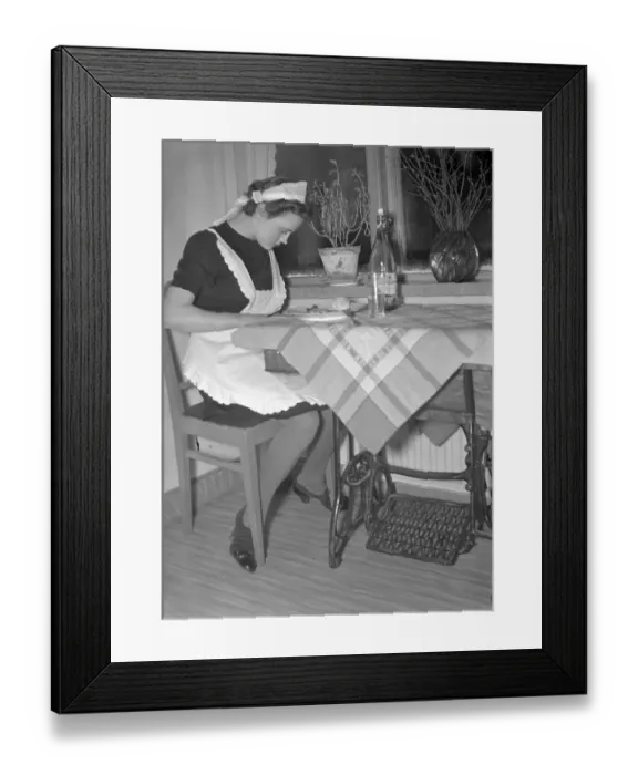 Framed Print : Living in the 1940s. A young woman working as a maid and the photographer followed her during a work day, here pictured when eating her lunch, but still at the sewing machine. Sweden 1940. Kristoffersson ref 56-1