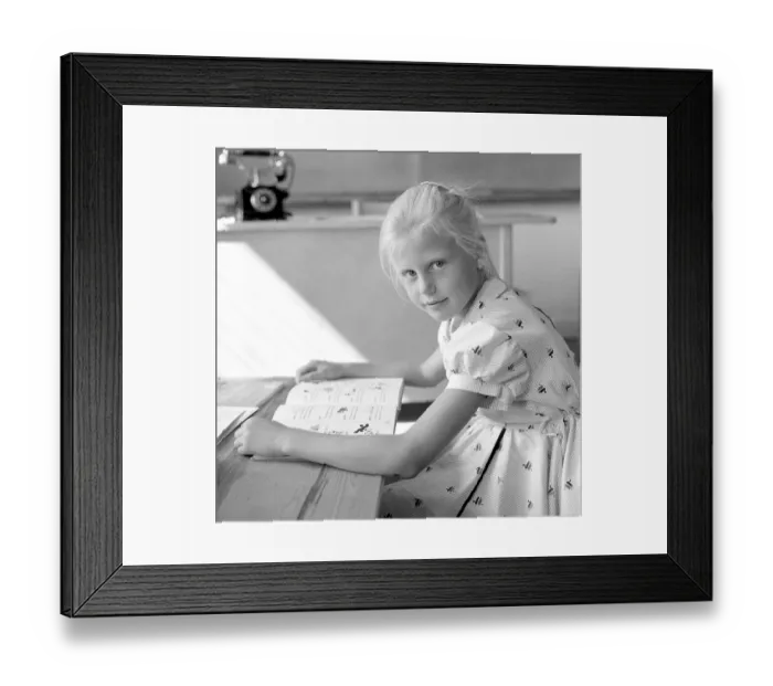 Framed Print : School in the 1950s. A girl is seen sitting at her desk in the classroom reading from the schoolbook in front of her