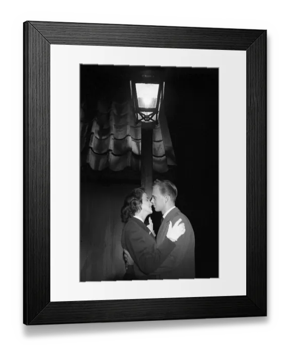 Framed Print : Love in the 1950s. A young couple in the evening are standing under a street lamp kissing Framed Print : Love in the 1950s. A young couple in the evening are standing under a street lamp kissing
