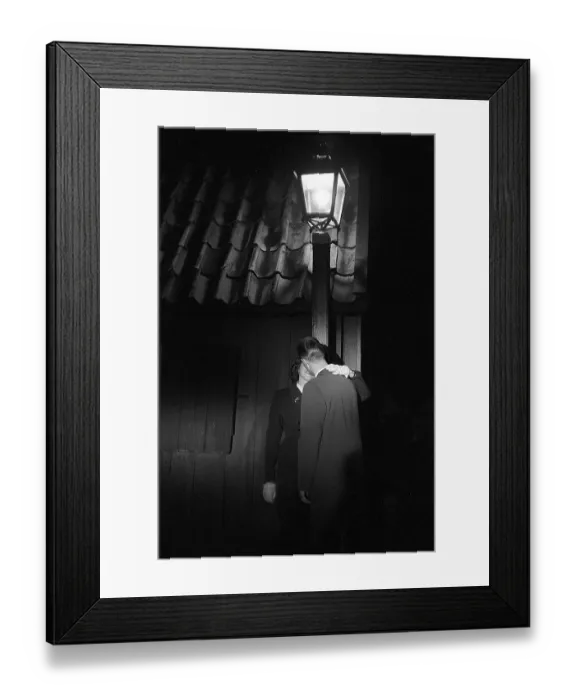 Framed Print : Love in the 1950s. A young couple in the evening are standing under a street lamp kissing Framed Print : Love in the 1950s. A young couple in the evening are standing under a street lamp kissing
